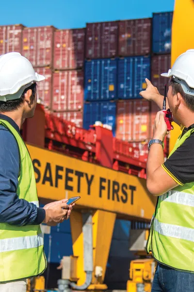Two males looking at the container ships in the distance. In front of them the crane says Safety First.