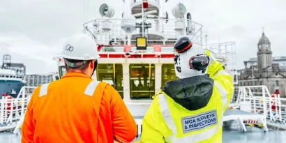 MCA Survey and inspection team member observes a vessel from the deck. They are wearing a yellow hi-visibility jacket and a white hard hat