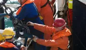 Seafarers at work on a vessel, wearing hi-vis and protective gear.