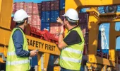 Two males looking at the container ships in the distance. In front of them the crane says Safety First.