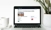 UK Ship Register Online Service web page on a laptop with a coffee cup to the left and a plant to the right